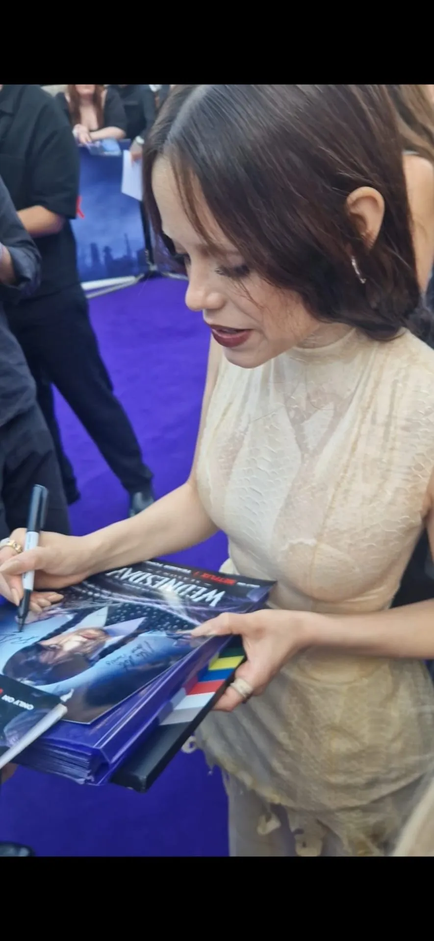 Jenna Ortega signing a Wednesday poster at a premiere